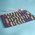 Rectangular wristlet clutch bag with psychedelic black, purple, red, and green pattern. White wrist strap and gold zipper visible